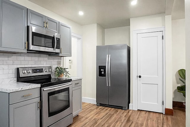 kitchen featuring appliances with stainless steel finishes, gray cabinets, tasteful backsplash, light wood-type flooring, and baseboards