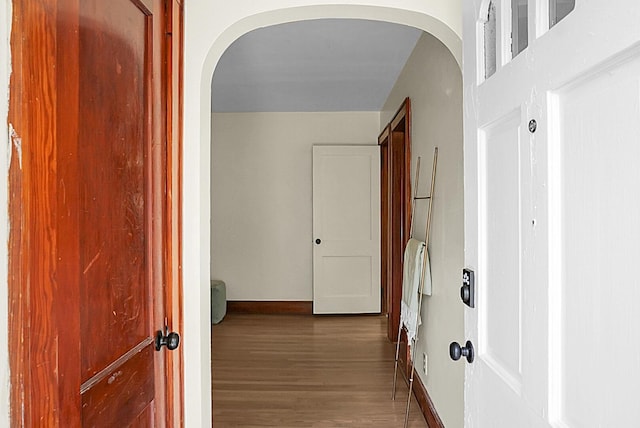 corridor with arched walkways, wood finished floors, and baseboards