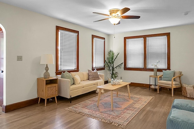 living room with arched walkways, ceiling fan, baseboards, and wood finished floors