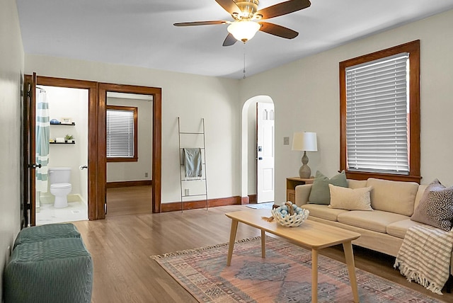 living area with arched walkways, a ceiling fan, light wood-style flooring, and baseboards