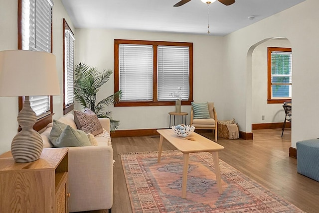 living room with arched walkways, wood finished floors, a ceiling fan, and baseboards