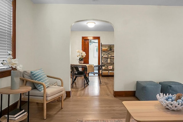sitting room featuring arched walkways, light wood-style floors, and baseboards