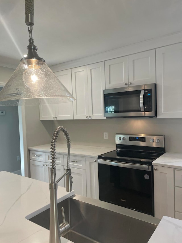 kitchen with appliances with stainless steel finishes, pendant lighting, light stone counters, and white cabinetry