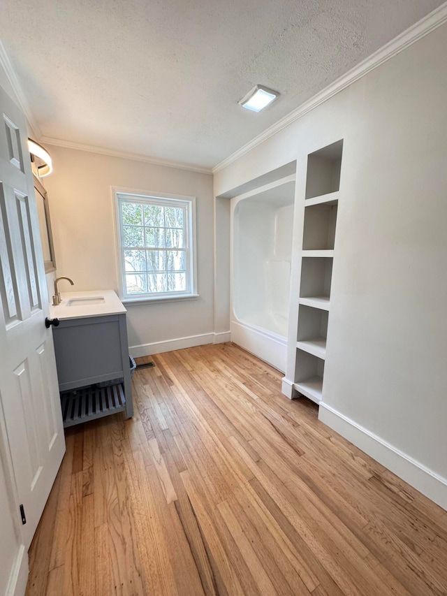 interior space featuring crown molding, sink, light hardwood / wood-style floors, and a textured ceiling