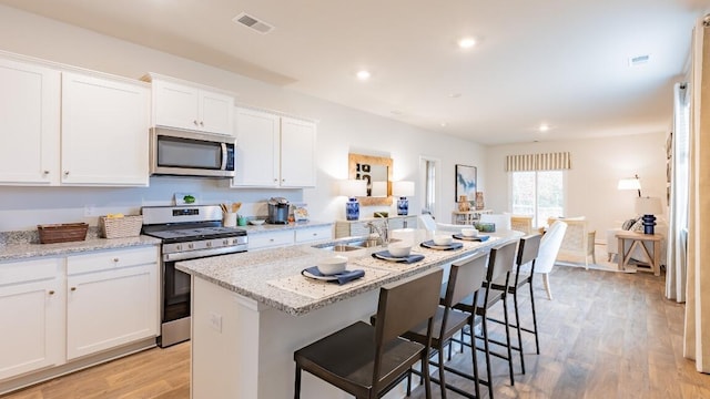 326 Watersglen Dr, Summerville, SC 29486 - kitchen with stainless steel appliances, a sink, white cabinetry, light wood-style floors, and an island with sink