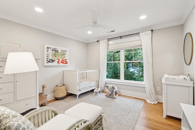 bedroom with a crib, ceiling fan, crown molding, and light wood-type flooring