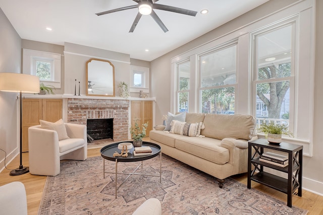 living room featuring a brick fireplace, ceiling fan, and light wood-type flooring