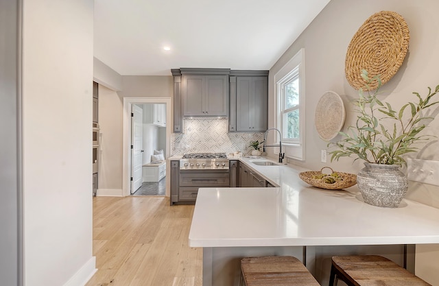 kitchen with gray cabinetry, sink, a kitchen breakfast bar, light hardwood / wood-style flooring, and kitchen peninsula