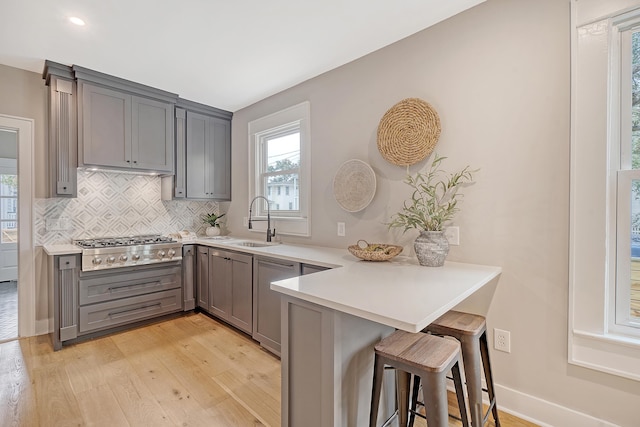 kitchen featuring kitchen peninsula, a breakfast bar, sink, light hardwood / wood-style floors, and stainless steel gas stovetop