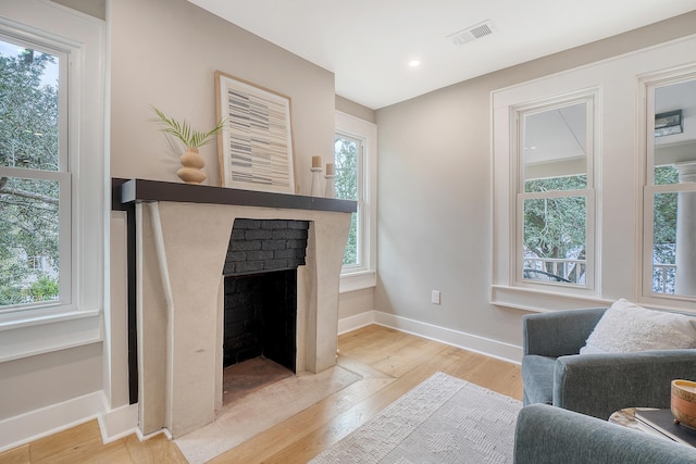 living room featuring a brick fireplace, light hardwood / wood-style flooring, and plenty of natural light