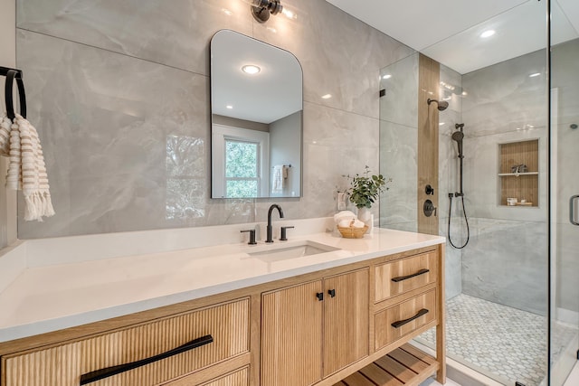 bathroom featuring a shower with door, vanity, and tile walls