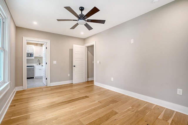 unfurnished bedroom with ceiling fan, light wood-type flooring, sink, and ensuite bath