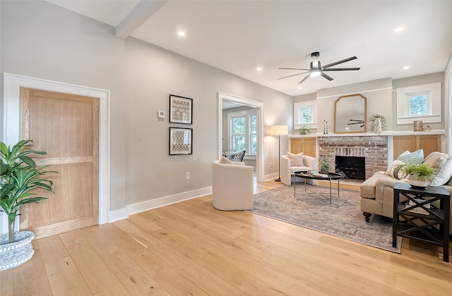 living room with ceiling fan, light hardwood / wood-style flooring, and a brick fireplace