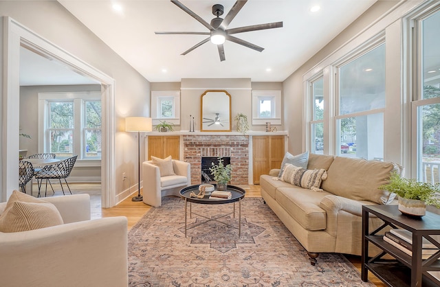 living room featuring ceiling fan, a fireplace, and light hardwood / wood-style floors