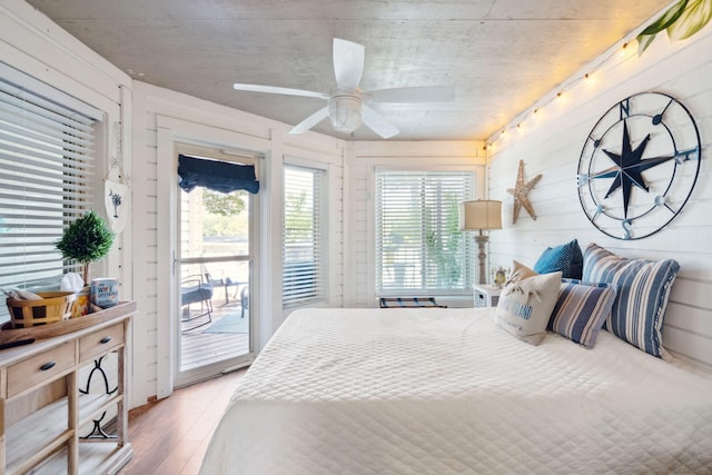 bedroom featuring wooden walls, hardwood / wood-style floors, ceiling fan, and access to outside