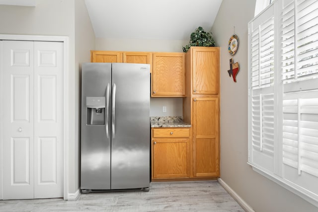 kitchen with light stone countertops, light wood-type flooring, and stainless steel refrigerator with ice dispenser