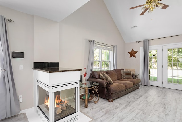 living room with light hardwood / wood-style flooring, a multi sided fireplace, ceiling fan, and high vaulted ceiling