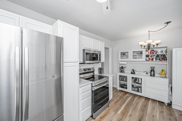 kitchen with a textured ceiling, stainless steel appliances, pendant lighting, and white cabinets