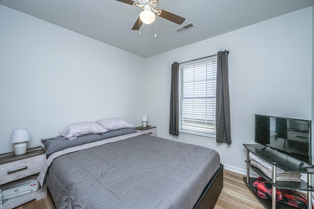 bedroom with a textured ceiling, ceiling fan, and light hardwood / wood-style floors