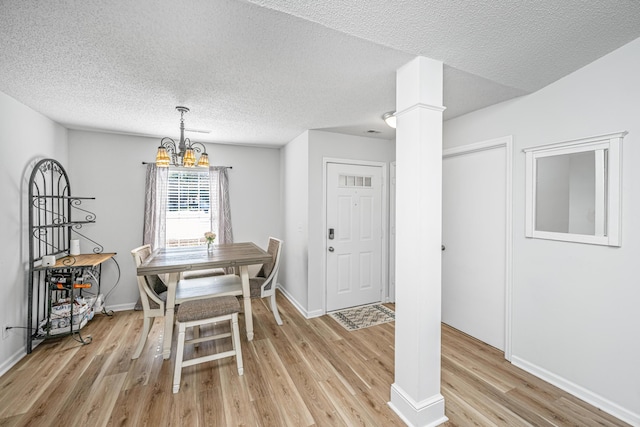 dining room featuring decorative columns, a textured ceiling, light hardwood / wood-style flooring, and a notable chandelier