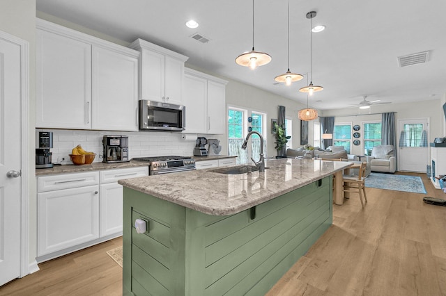 3789 Tupelo Branch Row, Mount Pleasant, SC 29429 - kitchen with stainless steel appliances, light wood finished floors, a kitchen island with sink, white cabinets, and tasteful backsplash