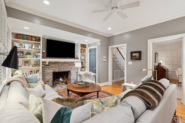 living room featuring a brick fireplace, built in features, light hardwood / wood-style floors, and ornamental molding