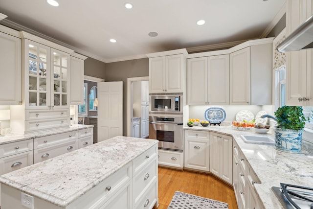 kitchen featuring stainless steel appliances, light stone countertops, ornamental molding, white cabinets, and sink