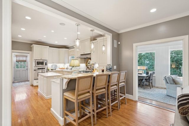 kitchen with kitchen peninsula, stainless steel appliances, a breakfast bar, white cabinets, and ornamental molding