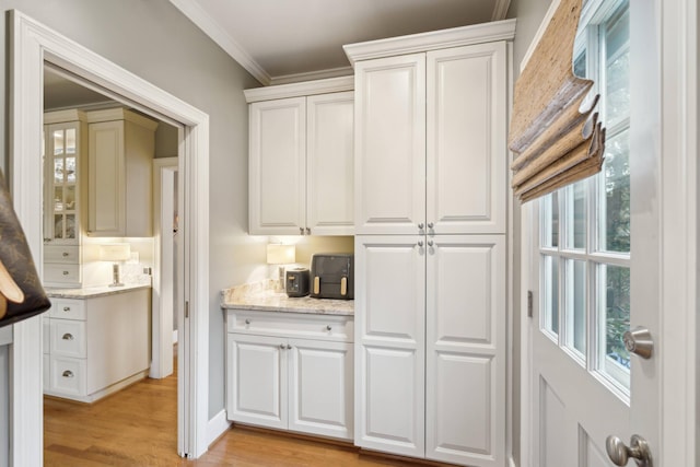 kitchen featuring white cabinets, light hardwood / wood-style floors, ornamental molding, and light stone counters