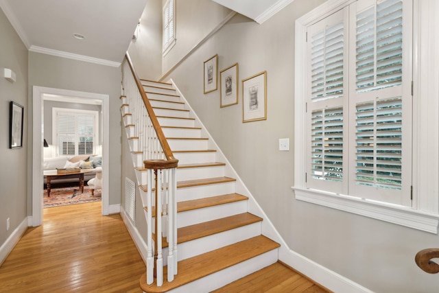 stairway with a healthy amount of sunlight, hardwood / wood-style flooring, and crown molding