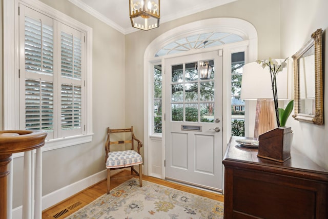 foyer featuring a healthy amount of sunlight, light wood-type flooring, ornamental molding, and an inviting chandelier