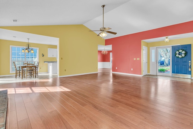 unfurnished living room featuring lofted ceiling, ceiling fan with notable chandelier, wood finished floors, and a wealth of natural light