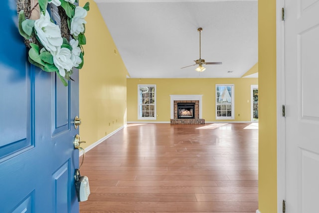 entryway featuring a brick fireplace, vaulted ceiling, ceiling fan, wood finished floors, and baseboards