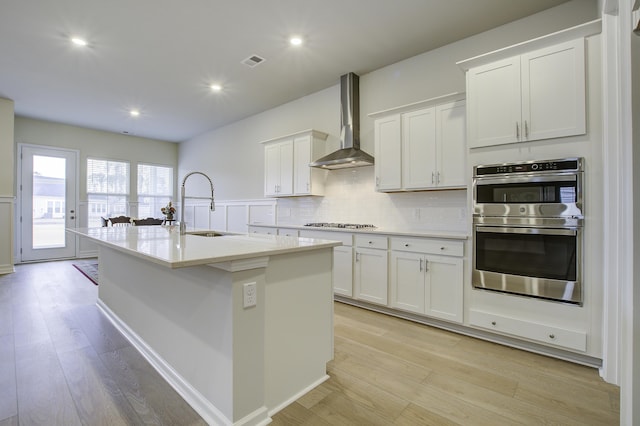 kitchen featuring white cabinets, sink, wall chimney exhaust hood, an island with sink, and stainless steel appliances