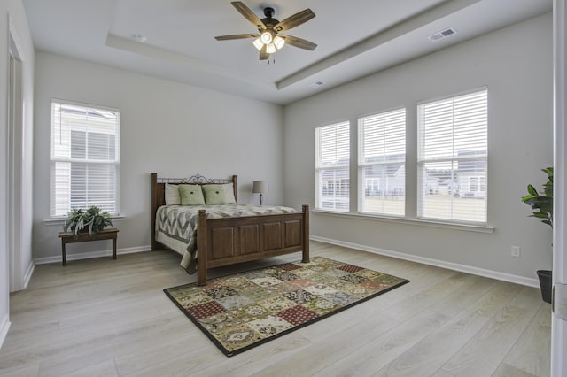 bedroom with ceiling fan, a raised ceiling, and light hardwood / wood-style flooring