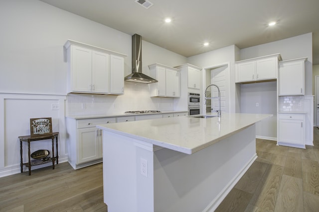 kitchen featuring a center island with sink, white cabinets, sink, wall chimney exhaust hood, and light wood-type flooring