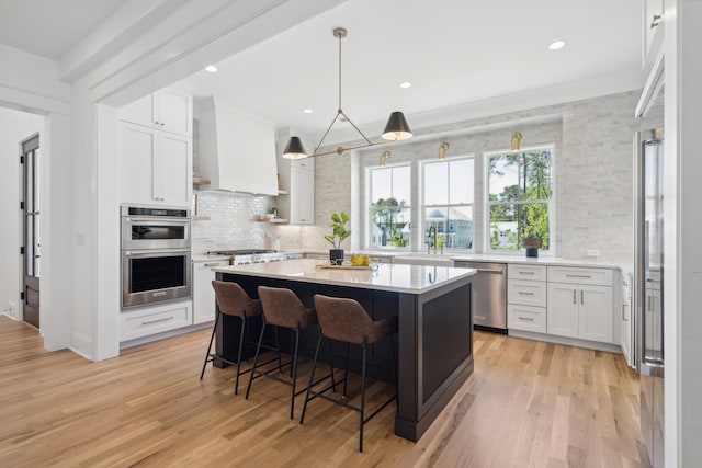 kitchen with a kitchen bar, light wood-style flooring, stainless steel appliances, white cabinets, and light countertops