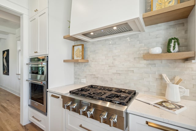 kitchen with white cabinets, light stone countertops, light wood-type flooring, stainless steel appliances, and tasteful backsplash