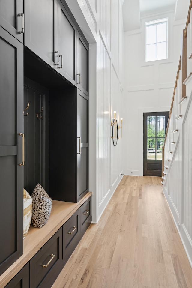 mudroom featuring light wood finished floors, a decorative wall, and a high ceiling