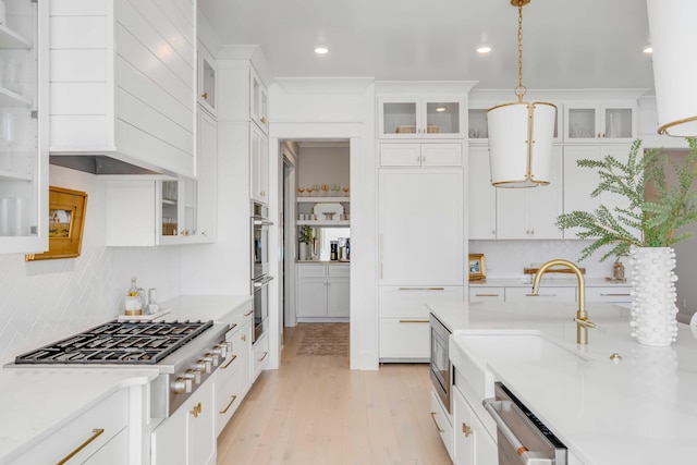 kitchen with sink, appliances with stainless steel finishes, hanging light fixtures, white cabinets, and light wood-type flooring