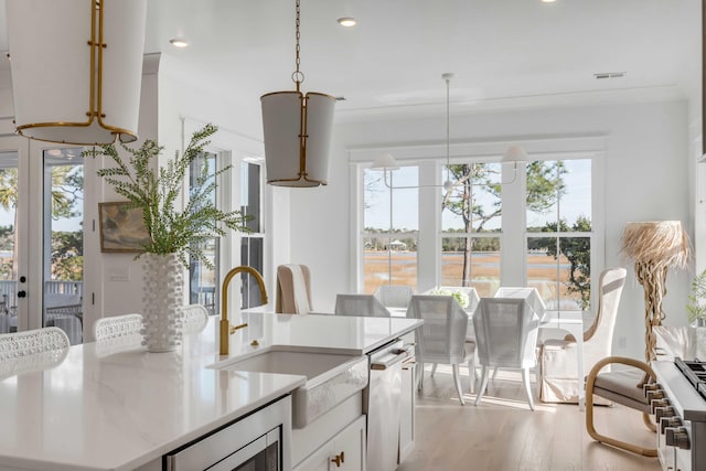 kitchen featuring sink, light hardwood / wood-style flooring, hanging light fixtures, ornamental molding, and white cabinets