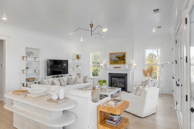 living room featuring a notable chandelier, crown molding, a fireplace, and light hardwood / wood-style floors