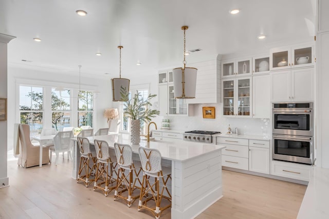 kitchen featuring decorative light fixtures, a center island with sink, backsplash, appliances with stainless steel finishes, and white cabinets