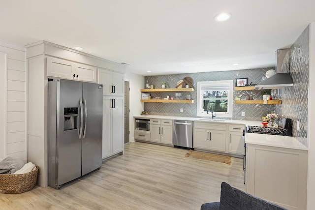 kitchen featuring open shelves, a sink, wall chimney range hood, appliances with stainless steel finishes, and light countertops