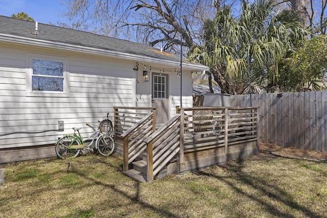 doorway to property with a shingled roof, a yard, fence, and a wooden deck