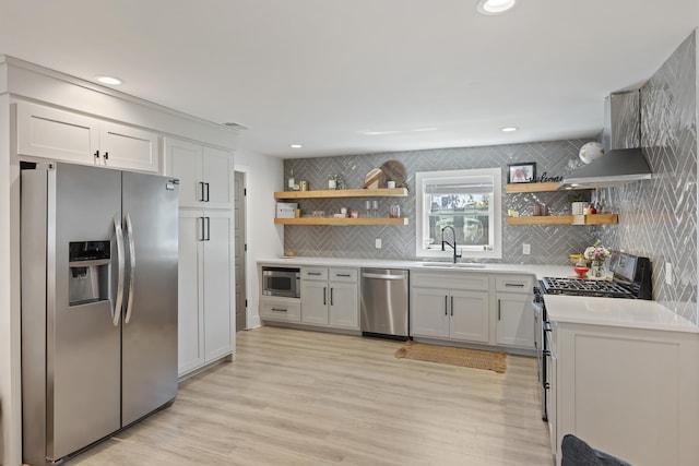 kitchen featuring open shelves, appliances with stainless steel finishes, wall chimney exhaust hood, and a sink