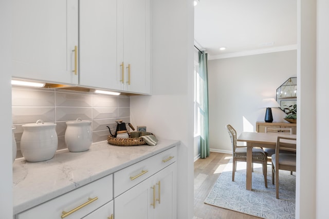 kitchen featuring white cabinetry, tasteful backsplash, ornamental molding, light stone countertops, and light hardwood / wood-style floors