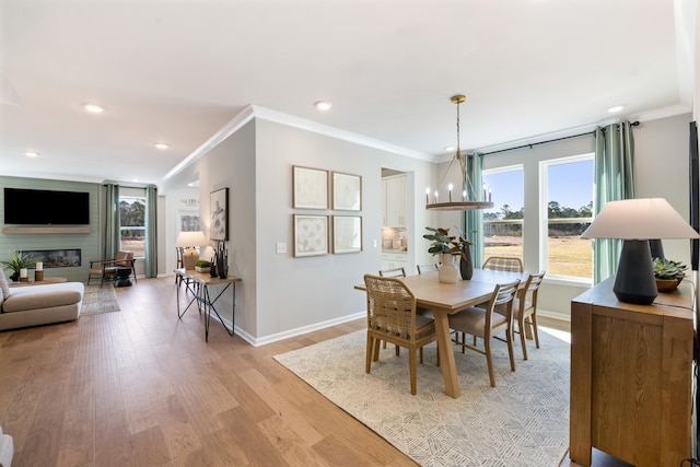 dining area with ornamental molding, a fireplace, light hardwood / wood-style flooring, and a notable chandelier