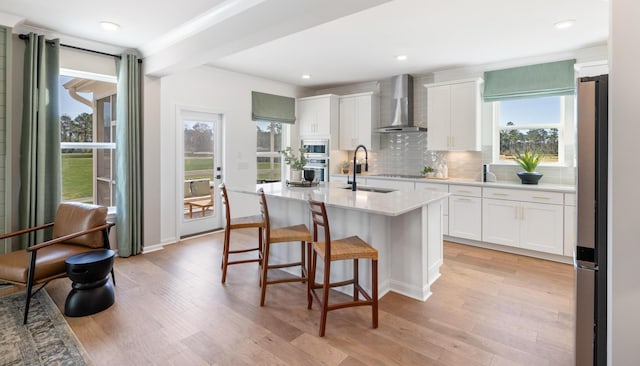 kitchen with a kitchen island with sink, wall chimney range hood, white cabinets, and appliances with stainless steel finishes