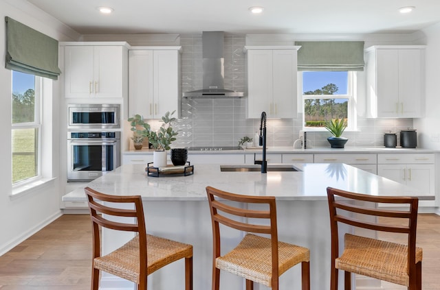 kitchen with appliances with stainless steel finishes, sink, white cabinets, backsplash, and wall chimney exhaust hood